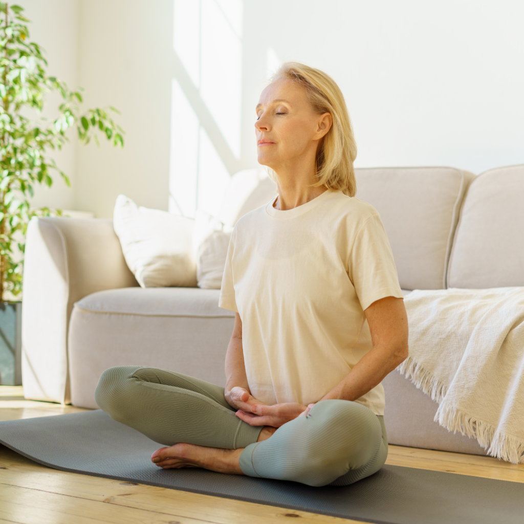 Retired woman meditating and practicing yoga while sitting in lotus pose on floor at home
